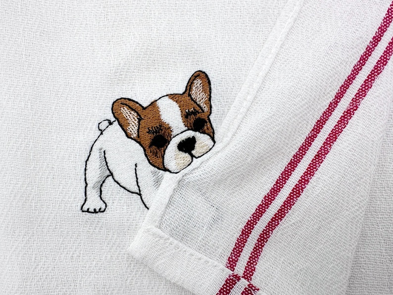 K&ouml;nnte beinhalten: Wei&szlig;es K&uuml;chentuch mit einem gestickten French Bulldog. Der Hund ist wei&szlig;, braun und schwarz. Das Handtuch hat zwei rote Streifen am Rand.