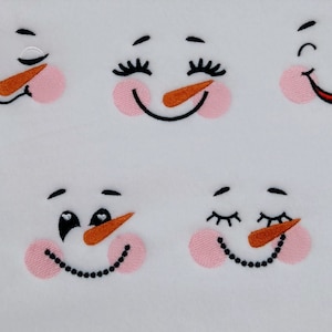 Puede incluir: Seis caras de muñeco de nieve bordadas con diferentes expresiones, incluyendo ojos cerrados, sonriendo y guiñando un ojo. Cada cara tiene un rubor rosado, una boca negra y una nariz de zanahoria naranja.