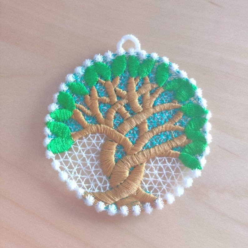 May include: A round, white, crocheted ornament with a gold tree design and green leaves. The ornament has a loop at the top for hanging.