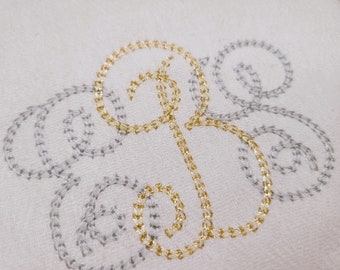 May include: A white fabric with a gold and silver embroidered design. The design is a stylized letter "B" with swirls.