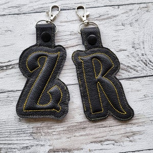 May include: Two black leather keychains with yellow stitching, shaped like the letters Z and R.