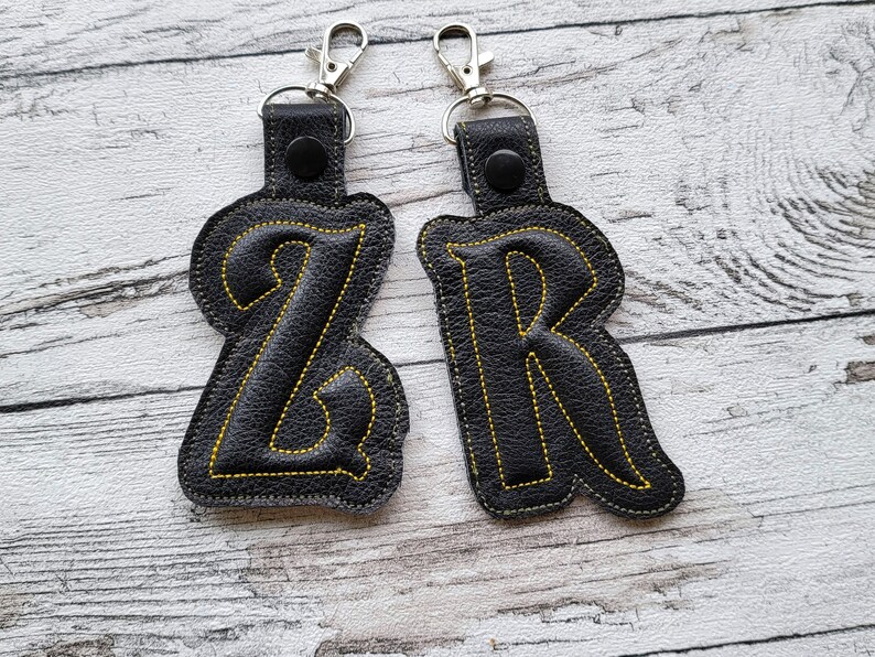 May include: Two black leather keychains with yellow stitching, shaped like the letters Z and R.