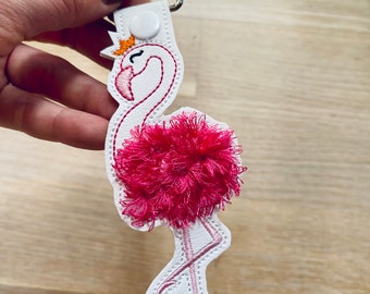 May include: A white leather flamingo keyring with a pink pom-pom for the feathers and a silver metal key ring.