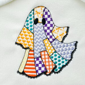 May include: Embroidered ghost applique with a patchwork design. The ghost features various patterns, including hearts, zigzags, and checks, in orange, purple, teal, and yellow. The edges are trimmed with black lace.