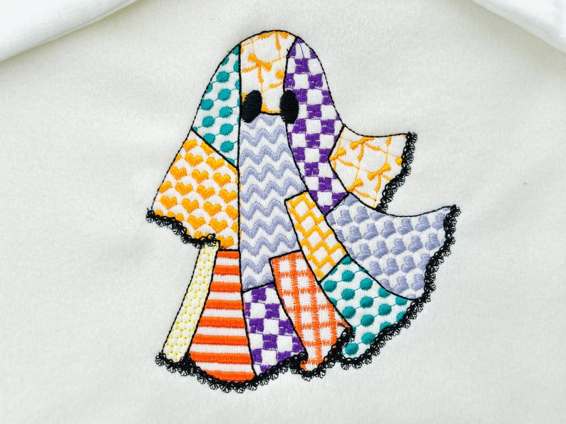 May include: Embroidered ghost applique with a patchwork design. The ghost features various patterns, including hearts, zigzags, and checks, in orange, purple, teal, and yellow. The edges are trimmed with black lace.
