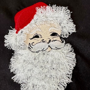 Op de afbeelding: Geborduurde kerstman gezicht met een rode muts en witte baard. Het gezicht glimlacht met een witte baard en snor.