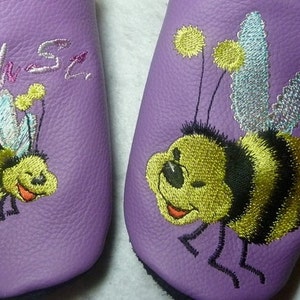 May include: A pair of purple leather slippers with embroidered bumblebees. One slipper has the word "wah-sz" embroidered on it.