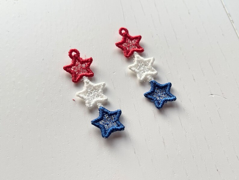 Pu&ograve; includere: Un paio di orecchini con tre stelle ciascuno. Le stelle sono rosse, bianche e blu.