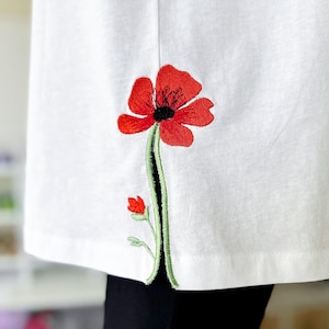 May include: White t-shirt with a red embroidered poppy flower on the side seam.