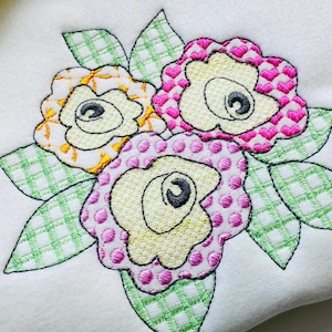 May include: Embroidered design of three flowers with green leaves. The flowers are yellow, pink, and white with different patterns.