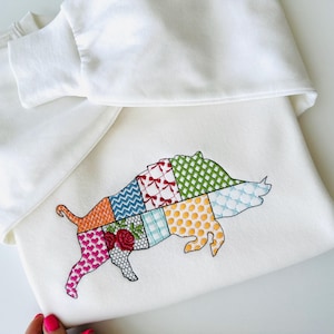 May include: White sweatshirt with a colorful embroidered patchwork boar design.