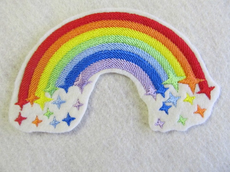 May include: A rainbow-colored embroidered patch with a white background and stars. The rainbow is made of red, orange, yellow, green, blue, indigo, and violet. The stars are white, yellow, orange, and blue.
