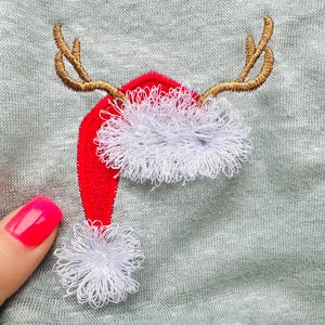 May include: Embroidered design of a red Santa hat with white trim and brown reindeer antlers on a gray fabric background.