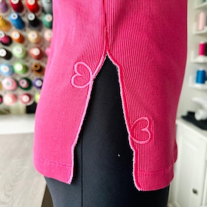Könnte beinhalten: Ein rosa geripptes Tanktop mit einem Seitenschlitz und weißer Herzstickerei.