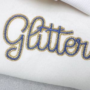 Puede incluir: Primer plano de la palabra "Glitter" bordada en purpurina dorada con un contorno azul sobre tela blanca. Un lazo blanco es visible en la esquina superior derecha. El diseño es probablemente para una manualidad o accesorio.
