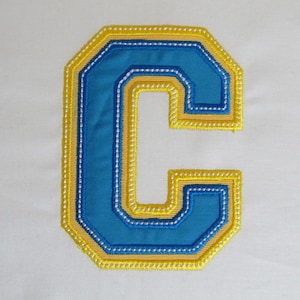 May include: A blue and yellow felt letter C with a stitched outline. The letter is a decorative patch or applique.