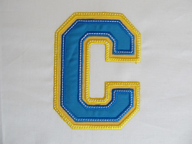 May include: A blue and yellow felt letter C with a stitched outline. The letter is a decorative patch or applique.