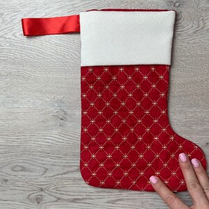 Peut inclure: Chaussette de Noël rouge avec un revers blanc et un motif en losanges dorés. La chaussette a une boucle de ruban rouge en haut.