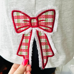 May include: A red and green plaid bow with white fringe, embroidered on a gray fabric.