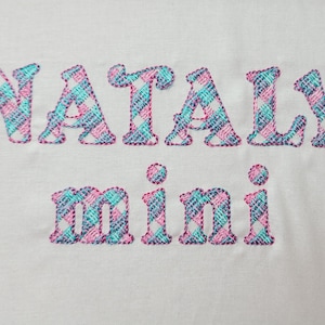 Puede incluir: Tela blanca con el nombre "NATALY" y la palabra "mini" bordada en cuadros rosa y azul.