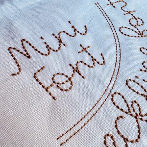 May include: White fabric with brown embroidery that reads "Mini Font Design".
