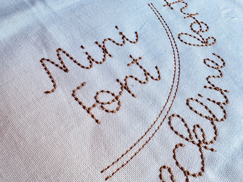 May include: White fabric with brown embroidery that reads "Mini Font Design".