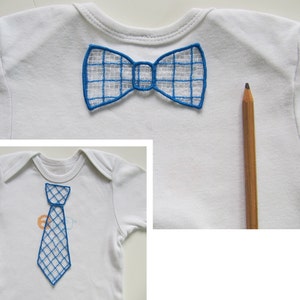 Puede incluir: Dos bodies blancos para bebé con diseños bordados en azul. Un body tiene una pajarita y el otro una corbata.