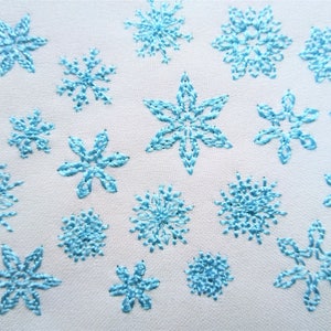 May include: A white fabric background with a scattered pattern of blue embroidered snowflakes of various sizes and styles.