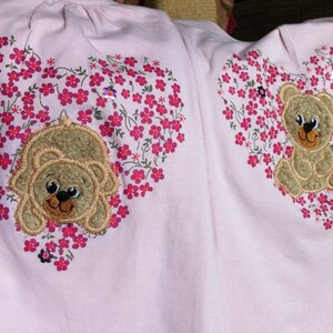 May include: Two pink shirts with embroidered hearts featuring brown teddy bears and pink flowers.