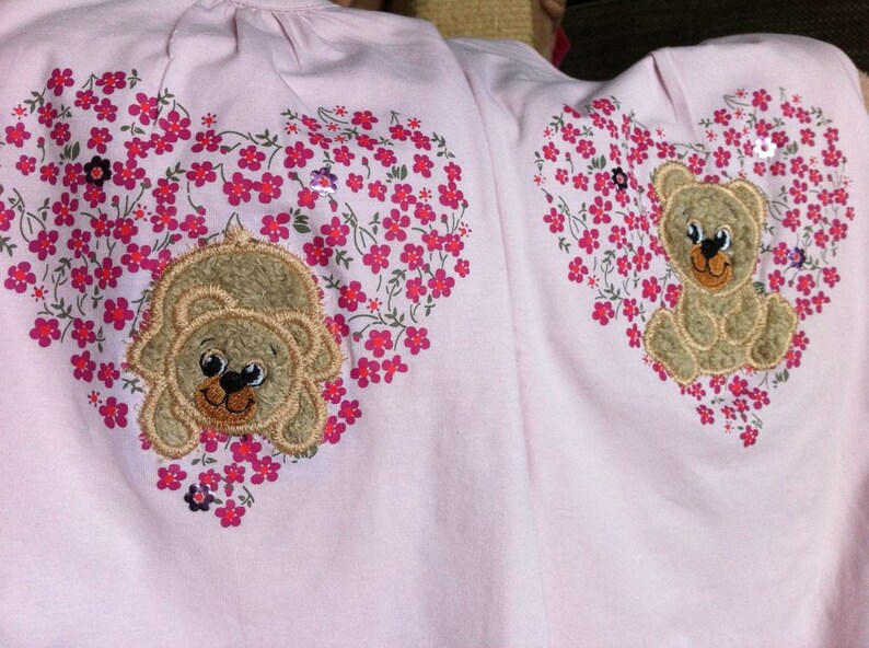 May include: Two pink shirts with embroidered hearts featuring brown teddy bears and pink flowers.