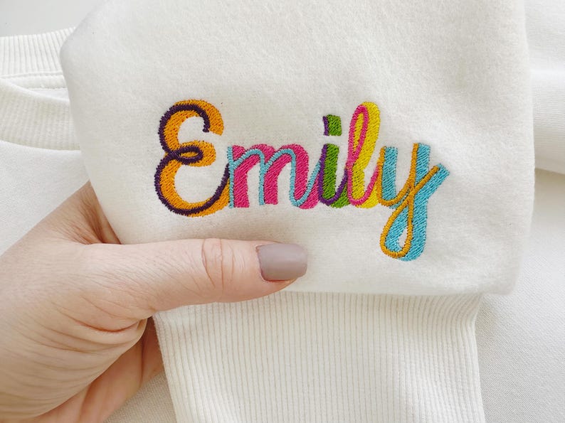May include: White sweatshirt with the name "Emily" embroidered in colorful thread.