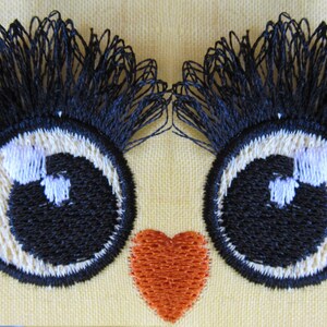 May include: Two black embroidered eyes with white highlights and long black eyelashes, and a red heart embroidered on a yellow fabric.