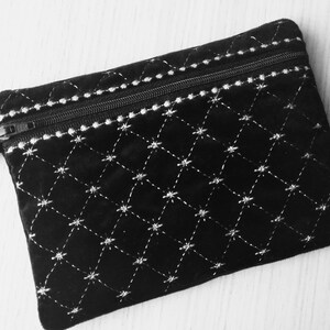 May include: A black velvet zippered pouch with a white diamond pattern and a black strap.