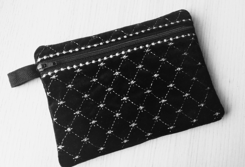 May include: A black velvet zippered pouch with a white diamond pattern and a black strap.