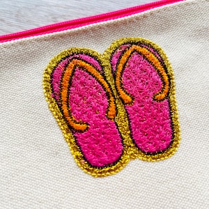 May include: A white canvas zippered pouch with a pink and orange embroidered design of two flip flops.