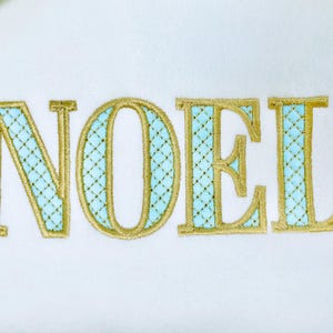 May include: Embroidered word "NOEL" in gold thread with a light blue cross-stitch pattern on a white background. The letters are large and stylized, suitable for festive decorations.