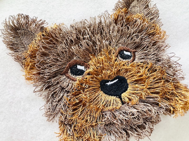 Puede incluir: Primer plano de un rostro de perro Yorkshire Terrier bordado en marr&oacute;n y beige con ojos y nariz negros.
