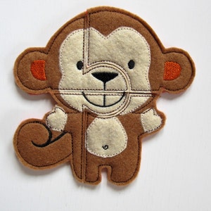 May include: A brown felt monkey puzzle with orange ears and a white face. The puzzle is made up of six pieces.