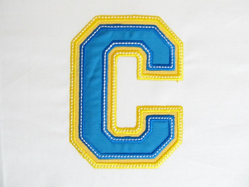 May include: A blue felt letter C with a yellow outline. The letter is stitched with white thread.