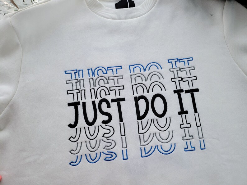 May include: White sweatshirt with a black and blue embroidered design that says "JUST DO IT" multiple times.