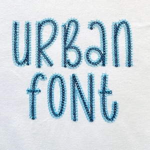Op de afbeelding: Geborduurde tekst in een blauw en lichtblauw lettertype dat "URBAN FONT" leest.