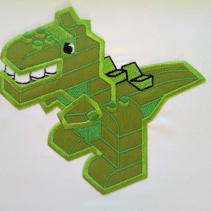 May include: Green embroidered patch of a cartoon dinosaur made of Lego blocks.