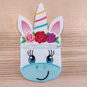 May include: White unicorn zipper pouch with a blue face, pink ears, and a rainbow horn. The unicorn has embroidered flowers on its head.