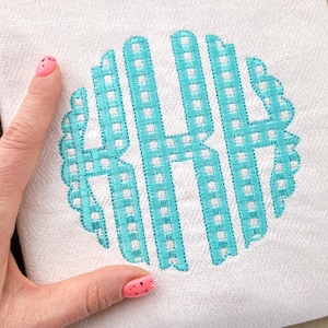 May include: A white towel with a turquoise blue monogram in a gingham pattern. The monogram is in a circle with a scalloped edge.