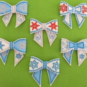 May include: Six decorative bows with snowflake designs. The bows feature white, light blue, and silver colours. Some bows have red snowflake accents. The bows are arranged on a green background.