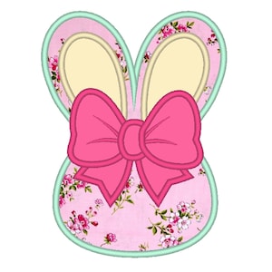 May include: A pink and floral bunny-shaped design with a large pink bow. The bunny ears and bow are outlined in a darker pink, with a light green border. The bunny's ears are a light yellow color.