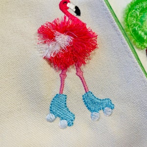 May include: Embroidered pink flamingo with white and pink pom-poms on its body, wearing blue roller skates with white wheels. The flamingo is on a white canvas background.