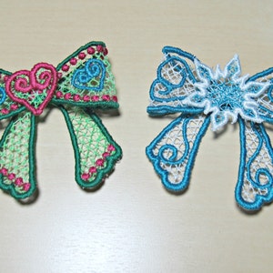 May include: Two embroidered lace bows, one green with pink hearts and one blue with a white snowflake.