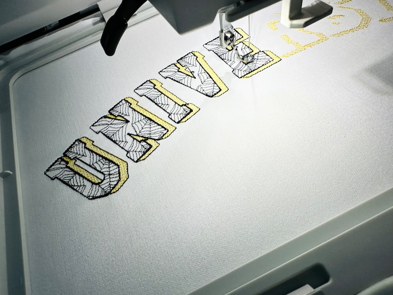 May include: A close-up of an embroidery machine stitching the word "UNIVE" in a yellow outline with a black and white patterned fill.