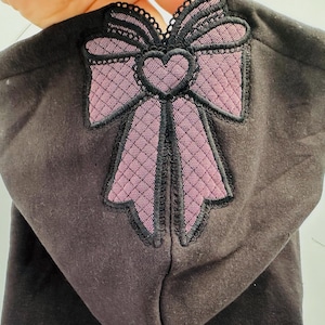 May include: Black hooded sweatshirt with a large pink and black bow applique on the front. The bow has a heart in the center.